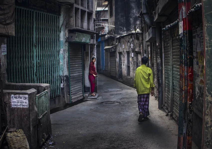 Two figures in a narrow street lined with closed shop shutters.