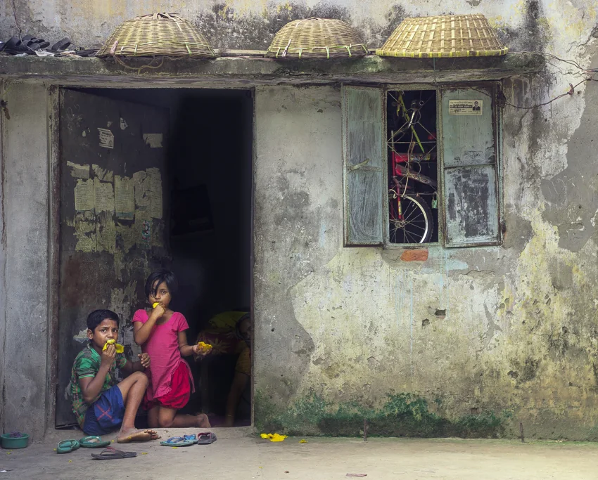 Two children sit in a doorway in a weathered building.